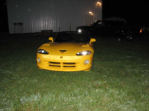 2001 Mercury Grand Marquis - A yellow sports car is parked on the grass at night, with a dark pickup truck in the background.