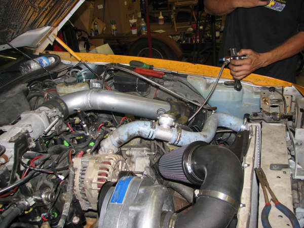 engine bay with aftermarket turbo and intake plumbing, person working on it