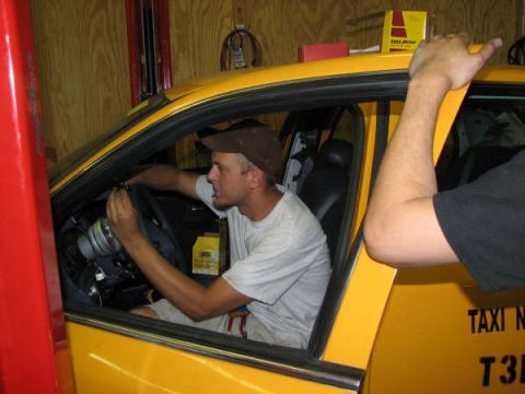 2001 Mercury Grand Marquis - A man works on the steering column of a yellow taxi, with "TAXI N" visible on the door.