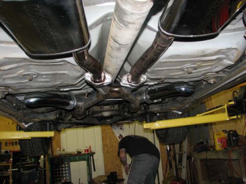 2001 Mercury Grand Marquis - The underside of a vehicle is shown, focusing on the dual exhaust system and mufflers, with a mechanic working nearby.