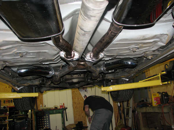 Underside of a car showing dual exhaust pipes and mufflers. A person is visible working below