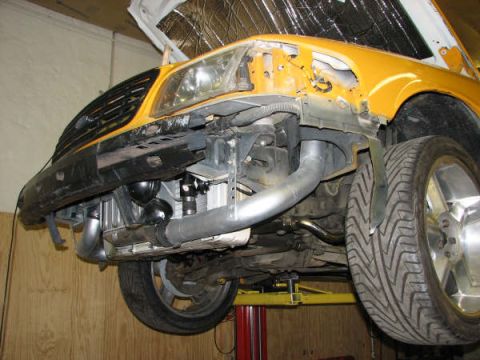 2001 Mercury Grand Marquis - Front view of a yellow vehicle undergoing modifications, with the hood raised to reveal engine components and custom piping.
