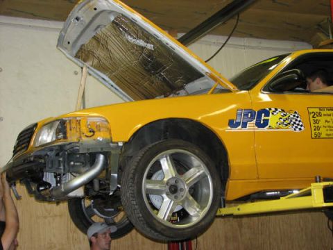 2001 Mercury Grand Marquis - Yellow taxi on a lift with its hood open and front bumper removed.