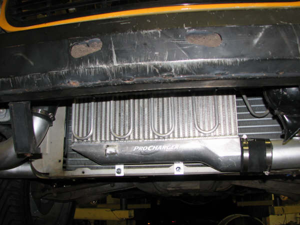 ProCharger intercooler mounted below a rusty bumper with yellow trim