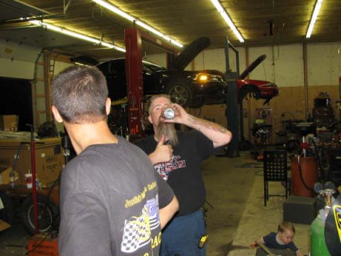 2001 Mercury Grand Marquis - Two men are in a cluttered garage with multiple vehicles being worked on, one car is on a lift.