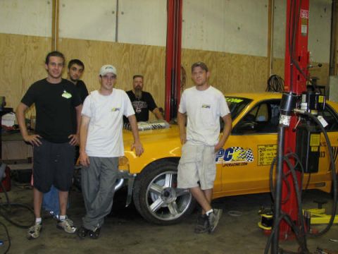 2001 Mercury Grand Marquis - A group of men stand with a yellow 2001 Mercury Grand Marquis, modified with racing decals and labeled as a taxi.