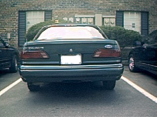 1994 Ford Taurus - Rear view of a dark sedan, possibly a 1992 model, parked in a lot with another vehicle nearby.
