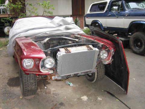 1969 Ford Mustang - A red car, possibly a 1969 Ford Mustang, is undergoing repairs with its hood open and radiator visible.