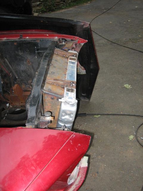 1969 Ford Mustang - Close-up view of a red vehicle's engine bay, focusing on the radiator and surrounding metal fabrication.