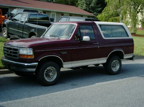 1992 Ford Bronco - This maroon Ford Bronco is parked on a residential street with other vehicles visible in the background.
