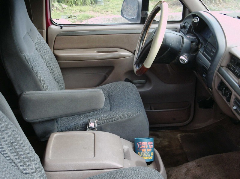 Bronco interior with gray cloth driver seat, tan console, wrapped steering wheel, and novelty cup in cup holder