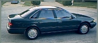 1994 Ford Taurus - A dark green sedan is parked on a street, viewed from the side. Another vehicle is in the background.