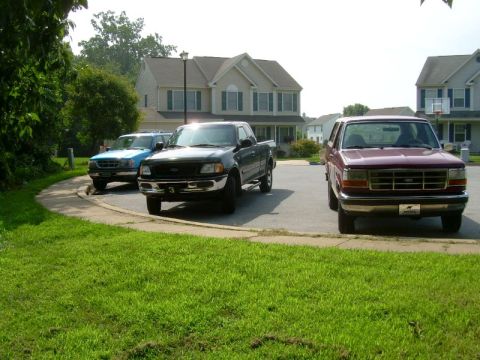 1992 Ford Bronco - Three Ford trucks, including a maroon F-250 and a black F-150, are parked in a residential driveway.
