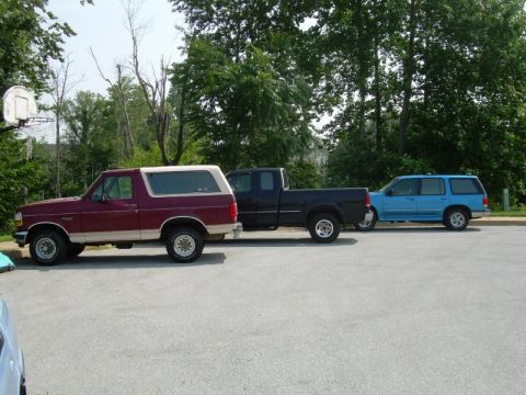 1992 Ford Bronco - A maroon and tan SUV is parked next to a black pickup truck and a blue SUV.