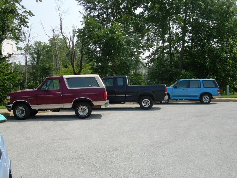 Maroon and tan SUV parked on asphalt, side view. Trees and a basketball hoop in background