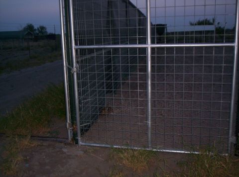 1986 Ford Bronco - A locked metal gate and enclosure are visible at dusk, with a dirt path and dry grass in the foreground.