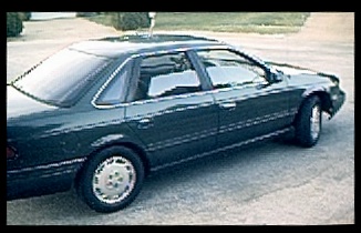 1994 Ford Taurus - This dark sedan is viewed from the rear passenger side, showing its body style and wheels.