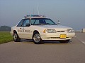 1993 Ford Mustang - A 1993 Ford Mustang police car is parked on the side of a road under a clear sky.