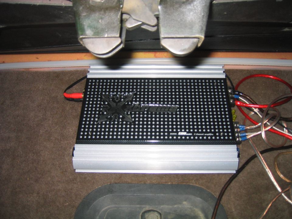 Xtreme 2-channel amplifier installed on brown carpet in vehicle cargo area with wiring attached