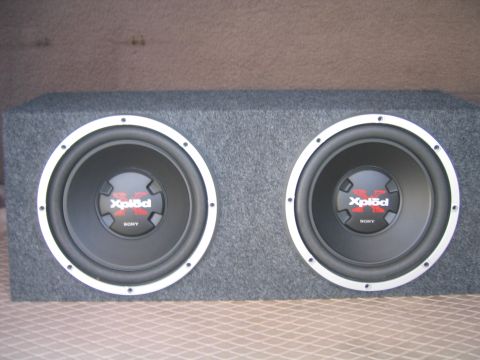 1996 Ford Bronco - A gray carpeted dual subwoofer enclosure holding two Sony Xplod subs with black cones, white trim rings and red logo dust caps, sitting on…