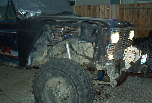 Front of a black Ford Bronco with its hood open, showing engine components. The grille and headlights are visible