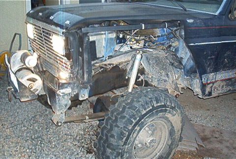 1986 Ford Bronco - The front end of a dark blue Ford Bronco shows significant damage, with the grille and headlights missing.