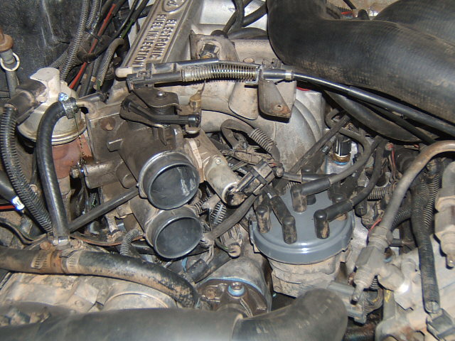 Close-up of engine bay showing throttle body with dual openings and a distributor cap with spark plug wires