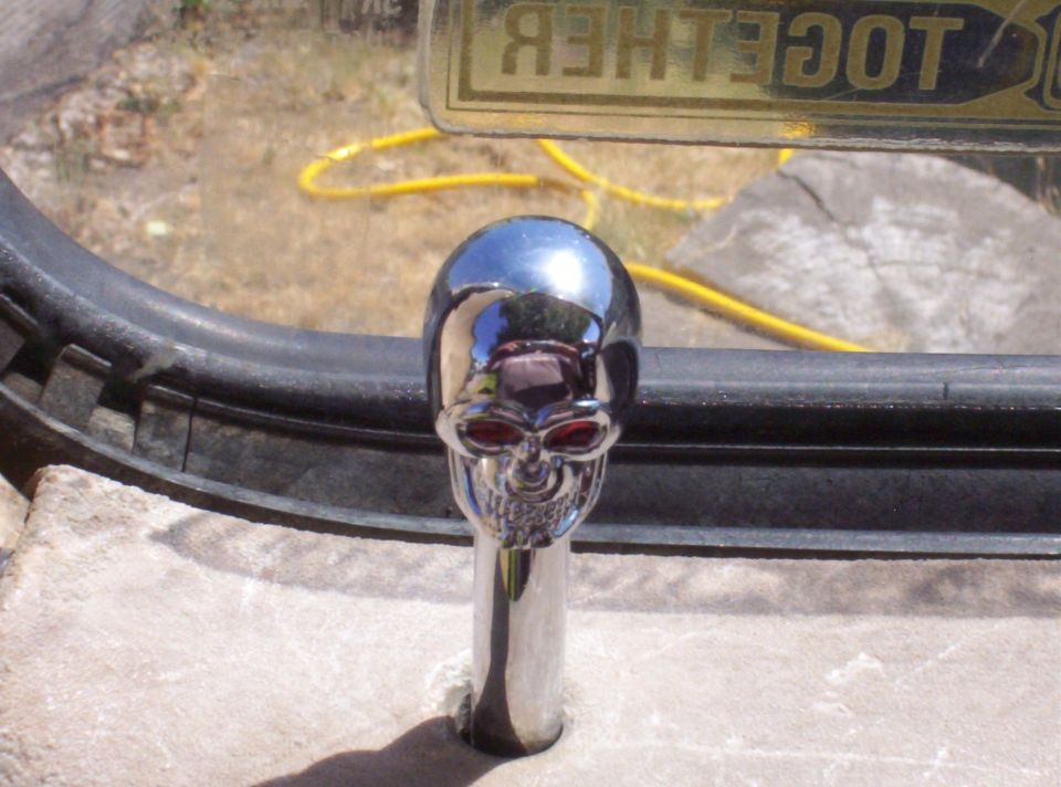 Chrome skull-shaped gear shift knob with red eyes mounted on a tire over rock