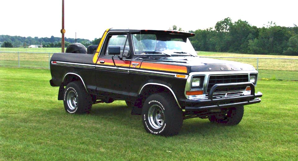 Black 1978 Ford Bronco with orange and yellow side stripes, chrome wheels, and a bull bar