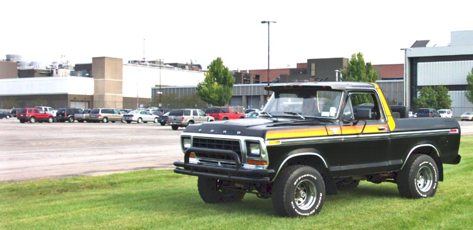 Black 1979 Ford Bronco with yellow and orange side stripes, parked on grass