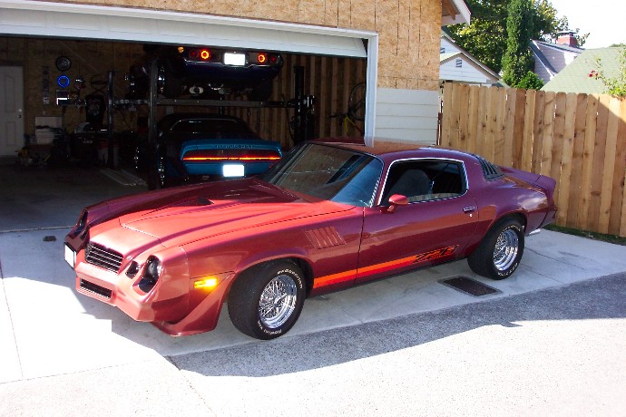 Red coupe with orange stripe, chrome wheels, and a spoiler parked in a driveway