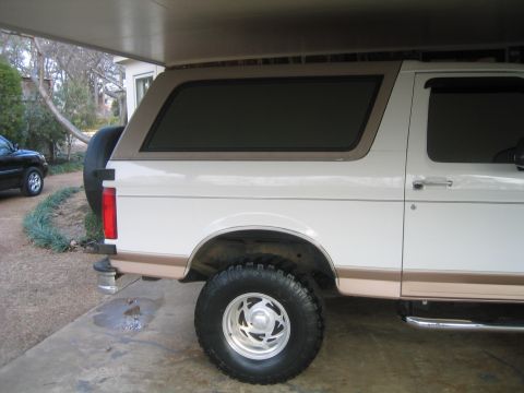 1996 Ford Bronco - Side view of a 1996 Ford Bronco parked under a carport, with another vehicle visible.