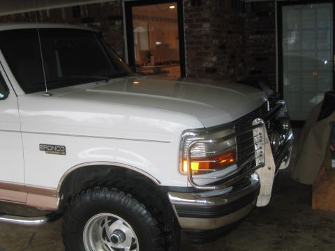 1996 Ford Bronco - The front corner of a white Ford Bronco is visible, showing its grille, headlights, and a portion of the tire.