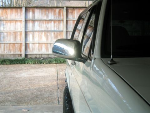 1996 Ford Bronco - The side mirror and part of the fender of a white SUV are visible against a wooden fence.