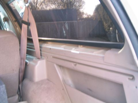 1996 Ford Bronco - The interior of the vehicle shows a beige seat and a seatbelt, with a view of the outside through the window.