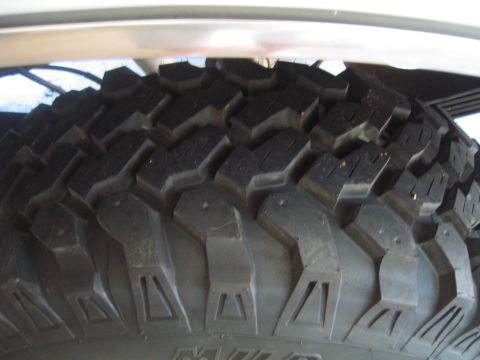 1996 Ford Bronco - Extreme close-up of a nearly new mud-terrain tire tread, showing the deep chunky lugs, siping and aggressive shoulder blocks with the sidew…