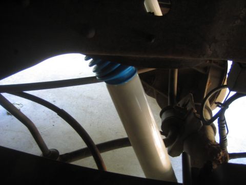 1996 Ford Bronco - Close-up under a lifted 4x4's front end showing a white-bodied shock absorber with a blue upper reservoir and ribbed boot bolted to the fra…