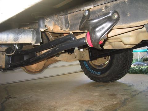 1996 Ford Bronco - Underbody view of a lifted 4x4's front suspension, showing a black radius arm running back to the frame, a red polyurethane coil spring iso…