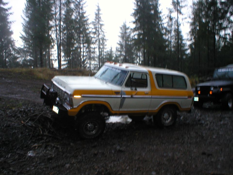 Lifted white and yellow Ford Bronco on muddy forest clearing, front three-quarter view