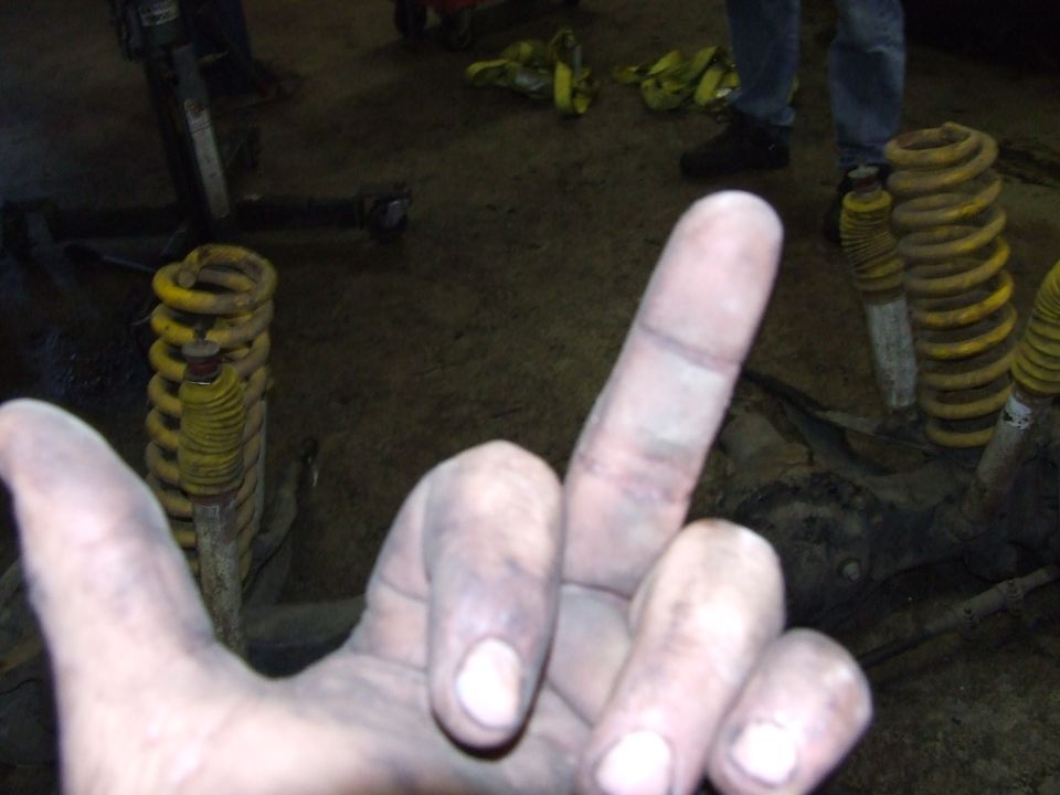 dirty hands in foreground, yellow coil springs and suspension components in background
