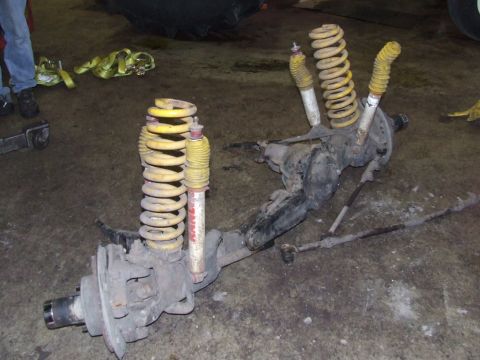 1986 Ford Bronco - A disassembled front axle assembly with shocks and springs is shown on a concrete floor.