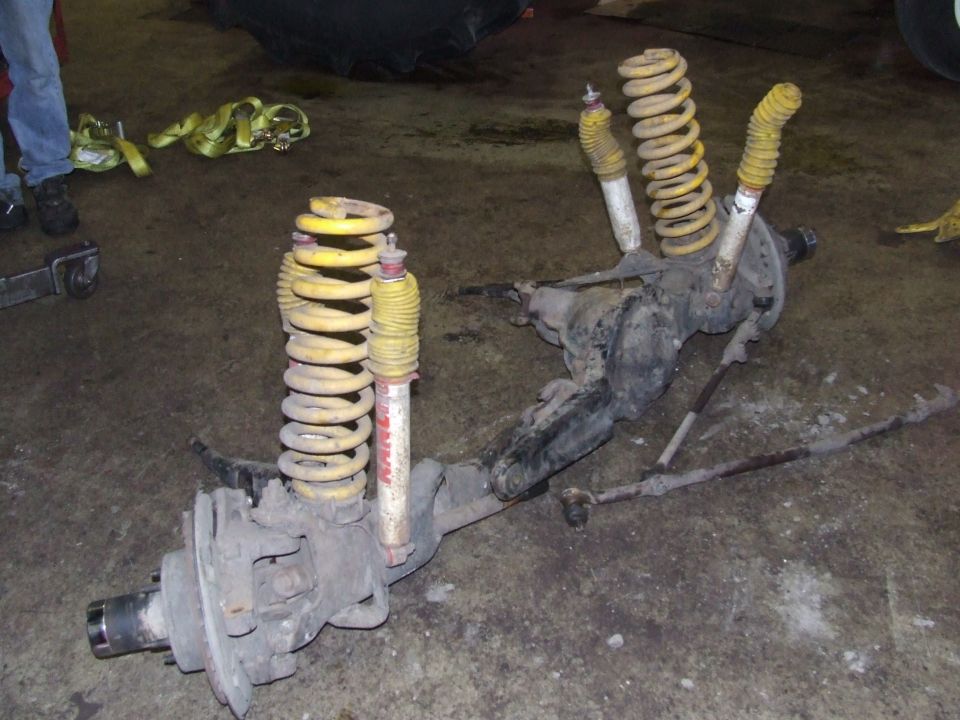 Front axle assembly with yellow springs and red/white shocks on concrete floor