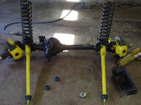 1986 Ford Bronco - Front axle assembly with yellow control arms, black springs, and shocks, likely for an off-road vehicle modification.