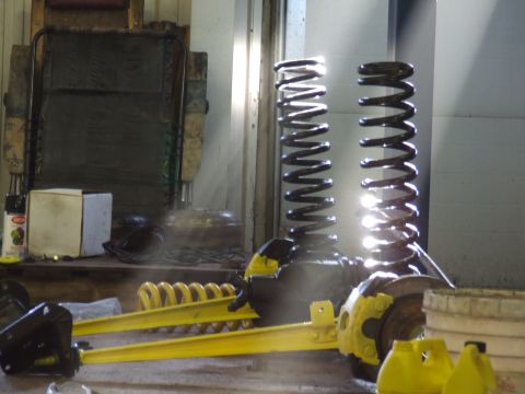 1986 Ford Bronco - Workshop scene with various automotive suspension parts, including coil springs and yellow-painted components.