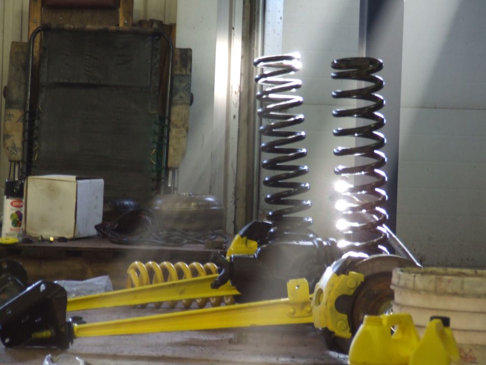 Two large black coil springs and yellow suspension components on a workshop floor