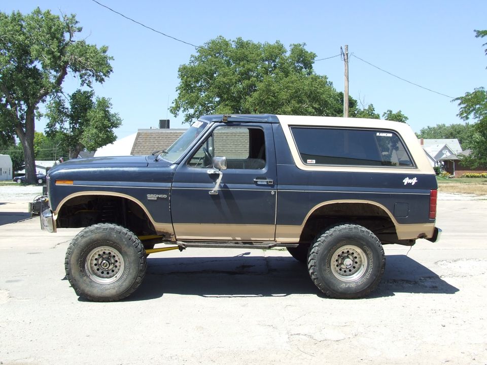 Blue and tan Ford Bronco with lifted suspension and large tires, seen from the side