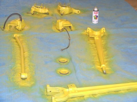 1986 Ford Bronco - Vehicle suspension parts are laid out and spray painted yellow on a blue tarp.