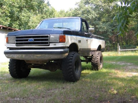 1989 Ford F-150 - This lifted pickup truck features a two-tone blue and white paint scheme and aggressive off-road tires.