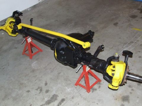 1986 Ford Bronco - Rebuilt solid front axle assembly sitting on red jack stands on a concrete garage floor, painted gloss black with a yellow-painted tie rod,…