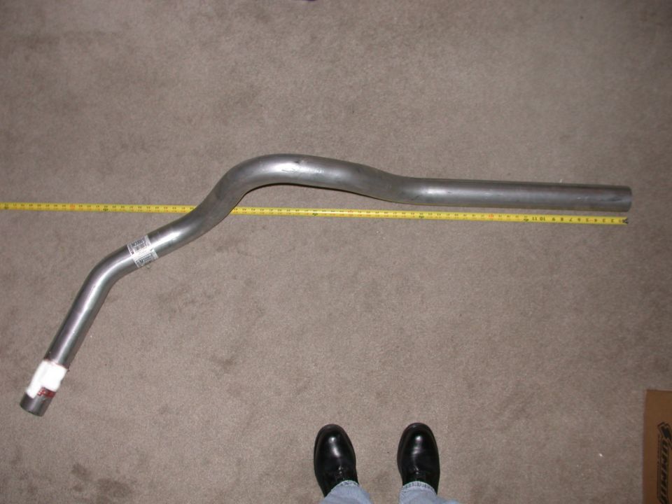 Bent stainless exhaust tailpipe on carpet next to a yellow tape measure